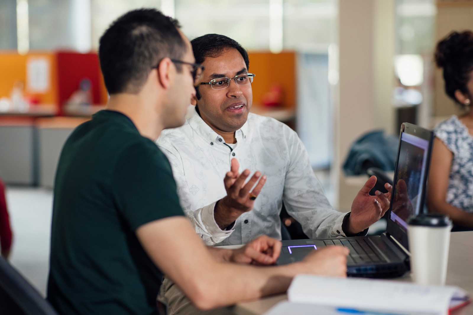 Two individuals having discussions at a laptop screen
